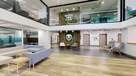 Located at 8204 Baltimore Ave in College Park, Maryland, this contemporary lobby serves as the welcoming centerpiece of the building. The space spans a generous single floor and immediately impresses with its soaring double-height ceilings and an open mezzanine level above, enclosed by glass railings and branded with an "Enjoy the View" sign — offering a dynamic sense of vertical space and transparency throughout.

The main floor features a blend of light wood-plank flooring and large-format gray tile, creating distinct zones within the open-plan layout. A staffed front desk with natural wood accents and built-in cabinetry anchors the workspace area, equipped with workstations and ample counter space. Adjacent to the desk, a comfortable lounge area offers modular upholstered seating in soft blue and neutral tones, ideal for resident gatherings or informal meetings.

A striking nature-inspired feature wall constructed of bamboo and living greenery, centered with a branded shield logo, adds warmth and visual interest near the elevator bank. Multiple elevators provide convenient vertical access throughout the building. Near the main entrance, floor-to-ceiling glass doors and sidelights invite natural light deep into the lobby, while a secondary lounge nook with modern chairs provides an intimate seating option. The overall ambiance is bright, clean, and thoughtfully designed.