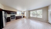 This well-appointed single-floor residence offers a thoughtfully designed open-concept layout that seamlessly connects the kitchen and living area. The kitchen is a standout feature, showcasing rich dark-espresso cabinetry with sleek hardware, light quartz countertops, and a full suite of stainless steel appliances including a refrigerator, electric range, over-the-range microwave, and dishwasher. Light-toned luxury vinyl plank flooring runs throughout the main living areas, lending a clean and contemporary feel.

The open living space is bathed in natural light, courtesy of multiple large windows dressed with horizontal blinds that frame views of surrounding greenery. A track lighting fixture overhead adds functional illumination to the kitchen zone.

The bedroom offers a comfortable and quiet retreat, finished with plush wall-to-wall carpeting and a generously sized window. The full bathroom is well-equipped with a dark-cabinetry vanity, white quartz countertop, large mirror, and a tiled shower-tub combination.

A dedicated in-unit laundry closet with washer and dryer hookups provides added convenience. Neutral warm-beige wall tones and consistent trim work throughout give the space a cohesive, move-in-ready aesthetic. The textured ceilings and clean architectural lines complete this practical yet stylish single-level home.