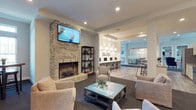 Located at 5793 Hoover Falls Dr in Westerville, Ohio, this single-floor community space is thoughtfully designed to offer both comfort and functionality. The main lounge area serves as the heart of the space, anchored by a striking floor-to-ceiling brick fireplace with a wood-burning insert and a wall-mounted flat-screen television above. Plush neutral-toned seating surrounds a vintage-style coffee table, creating an inviting atmosphere for relaxation and socializing. Recessed lighting and light gray walls contribute to a clean, contemporary aesthetic throughout. Adjacent to the lounge, a bar or café-style counter extends the gathering space, illuminated by a row of elegant pendant lights that add warmth and character. The counter area is ideal for casual dining or social interaction. Beyond the bar, a glass-enclosed room — likely a private dining or meeting space — is visible, featuring a chandelier and additional seating, offering a more formal setting for events or gatherings. Light wood-style flooring flows through the open-concept layout, tying the distinct zones together seamlessly. The overall ambiance balances a modern design sensibility with cozy, residential charm, making it a versatile and welcoming destination for residents and guests alike.