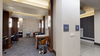 Located at 21525 Spring Plaza Dr in Spring, TX, this single-floor amenity suite offers a thoughtfully designed collection of spaces tailored for productivity and convenience. The layout includes a business center, a mail room, a private conference room, and a connecting hallway, all unified by a cohesive modern aesthetic.

The business center features a striking stacked-stone accent wall, warm walnut wood columns, and a marble-topped workstation paired with contemporary swivel seating. Ambient cove lighting above complements the patterned carpet flooring, creating a polished yet comfortable work environment.

The mail room is bright and functional, lined with a full wall of individual mailboxes set against a richly textured wallcovering. Large-format tile flooring, a marble-and-wood central island, and a sculptural pendant light give the space an elevated, boutique feel.

The private conference room is a standout, centered around a live-edge wood table surrounded by upholstered chairs. Natural light filters in through sheer floor-to-ceiling drapes, while a wall-mounted flat-screen TV, a blue-green tile accent wall, and lush potted greenery add character and warmth. Original artwork adorns the walls, enhancing the room's creative ambiance.

The hallway connecting these spaces is clean and bright, featuring large tile floors, a wall-mounted television, and framed artwork that adds a curated touch throughout.