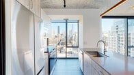 Located in Chicago's vibrant Old Town neighborhood, this three-bedroom, two-bathroom residence offers a thoughtfully designed single-floor layout with contemporary finishes throughout. The living area is a standout feature, anchored by expansive floor-to-ceiling windows and a distinctive exposed concrete ceiling, flooding the space with natural light while framing sweeping views of the Chicago skyline. Light-toned hardwood-style flooring runs throughout, complementing the clean, modern aesthetic. The kitchen is well-appointed with sleek cabinetry, stainless steel appliances including a built-in microwave and range, a tile backsplash, and a peninsula with a stone countertop and undermount sink — ideal for both cooking and entertaining. The primary bedroom is generously proportioned, featuring large floor-to-ceiling windows that capture impressive city views. Additional bedrooms are well-sized and equally bright, each with tall windows overlooking the surrounding cityscape. The bathrooms are finished with large-format tile flooring, dark wood vanities, backlit mirrors, and glass-enclosed showers. A dedicated laundry area houses a stacked washer and dryer unit, accompanied by a separate closet with wire shelving for added storage convenience.