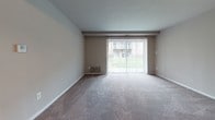 Located at 5214 Carswell Ave in Suitland, Maryland, this single-floor residence offers a straightforward and functional layout designed for comfortable everyday living. The main living area is carpeted and finished with neutral taupe-toned walls, providing a clean and versatile backdrop. A large sliding glass door fitted with vertical blinds fills the space with natural light and opens to a view of the surrounding outdoor greenery, adding a sense of openness to the room. A floor-level HVAC vent ensures climate control throughout.

The bedroom continues the carpeted flooring and neutral color palette, featuring a wide window with vertical blinds that allows natural light to filter in, creating a bright and airy atmosphere. The room offers ample wall space, providing flexibility for furniture arrangement.

The entryway transitions from carpet to hard-surface flooring and leads directly into the kitchen area, which is equipped with a full-size refrigerator and cabinetry. The kitchen connects seamlessly to the rest of the unit, supporting an efficient flow between spaces.

The bathroom is well-appointed with a full soaking tub and shower combination, a wood-toned vanity with a white countertop, an overhead mirror, and hard-surface flooring. The overall design of the residence is clean, practical, and move-in ready.