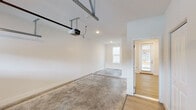 This single-floor space is centered around a spacious attached garage that offers generous room for vehicle storage and additional utility. The garage features a polished concrete floor, crisp white walls, recessed ceiling lighting, and a LiftMaster automatic garage door opener mounted on a ceiling track rail system. A built-in wall-mounted storage shelf adds practical organization options along one wall, while a textured ceiling completes the clean, functional aesthetic.

Directly accessible from the garage is a light-filled interior entry area that transitions seamlessly from the raw utility of the garage into the more finished living space. This transitional zone is finished with light-toned hardwood flooring and bright white walls, creating a welcoming and clean atmosphere. A glass-paneled exterior door allows natural light to pour in, offering views of the surrounding greenery outside.

A secondary interior doorway connects this entry area back to the garage, providing a clear and convenient flow between the two spaces. The overall design maintains a consistent, modern aesthetic throughout, with neutral tones, clean lines, and quality finishes. The space presents a well-organized, move-in ready layout that balances practicality with a polished appearance, making it well-suited for a variety of uses.