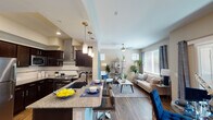 This single-floor residence is designed around an open-concept layout that seamlessly connects the kitchen, dining, and living areas into one cohesive, functional space. The kitchen is a standout feature, equipped with dark espresso cabinetry, stainless steel appliances including a full-size refrigerator and range, a statement stainless hood vent, granite countertops, and a deep undermount sink. Pendant lighting illuminates the kitchen island, which doubles as a breakfast bar with seating. Wood-style flooring extends throughout the main living area, contributing to a warm, unified aesthetic. The living room benefits from large windows that bring in generous natural light, complemented by a ceiling fan and access to an outdoor area via a sliding glass door. The bedroom features plush carpet, a ceiling fan, built-in wall shelving, and a charming window seat that adds both storage and character. Natural light filters in through a window dressed with curtains. The bathroom is elongated with wood-style flooring, a granite-topped vanity with dark cabinetry, and a walk-in shower area with a separate closet space, offering a practical and clean design throughout.
