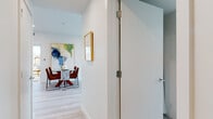 This thoughtfully designed single-floor residence showcases a clean, contemporary aesthetic throughout its well-connected living spaces. Light hardwood flooring flows seamlessly from room to room, complemented by crisp white walls that enhance the sense of openness and brightness.

The living area serves as the centerpiece of the home, featuring expansive floor-to-ceiling windows that frame sweeping urban rooftop views and flood the space with natural light. The kitchen is outfitted with glossy white cabinetry, light quartz countertops, a white subway tile backsplash, a stainless undermount sink, and an open wood floating shelf for display and storage.

Both bedrooms are intelligently designed with built-in, floor-to-ceiling white wardrobe systems that maximize storage while maintaining a sleek, uncluttered appearance. One bedroom benefits from large windows offering city views, while the other features a striking built-in surround unit framing the bed.

The bathrooms maintain the home's minimalist character, with large-format light tile flooring, floating white vanities, and backlit mirrors. A well-proportioned hallway connects the spaces, with curated artwork adding warmth and personality. Throughout, recessed lighting and a neutral palette create a calm, refined ambiance suited to modern living.