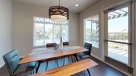 Located at 912 3rd Avenue in Chula Vista, CA, this single-floor community space is thoughtfully designed to encourage gathering and relaxation. The grand lounge serves as a centerpiece, boasting soaring double-height ceilings, hardwood-style flooring, and a classic white fireplace framed by a wall-mounted television. Generous windows and glass doors invite natural light while offering views of the surrounding outdoor area. An adjacent seating nook features plush accent chairs arranged for intimate conversation near large clerestory windows. The media and social lounge areas are carpeted and equipped with expansive dark leather sectional sofas, recessed lighting, and arched windows that lend architectural character. A well-appointed kitchen showcases soft blue-grey shaker cabinetry, white quartz countertops, rich hardwood-style floors, stainless steel appliances including a French door refrigerator, wall oven, built-in microwave, gas cooktop, and dishwasher, complemented by open floating shelves for added functionality. The dining area features a warm wood farmhouse-style table with hairpin legs, a matching bench, contemporary black chairs, and a striking layered drum pendant light, all bathed in natural light from multiple large windows overlooking lush greenery.