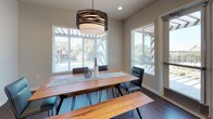 Located at 912 3rd Avenue in Chula Vista, CA, this single-floor community space is thoughtfully designed to encourage gathering and relaxation. The grand lounge serves as a centerpiece, boasting soaring double-height ceilings, hardwood-style flooring, and a classic white fireplace framed by a wall-mounted television. Generous windows and glass doors invite natural light while offering views of the surrounding outdoor area. An adjacent seating nook features plush accent chairs arranged for intimate conversation near large clerestory windows. The media and social lounge areas are carpeted and equipped with expansive dark leather sectional sofas, recessed lighting, and arched windows that lend architectural character. A well-appointed kitchen showcases soft blue-grey shaker cabinetry, white quartz countertops, rich hardwood-style floors, stainless steel appliances including a French door refrigerator, wall oven, built-in microwave, gas cooktop, and dishwasher, complemented by open floating shelves for added functionality. The dining area features a warm wood farmhouse-style table with hairpin legs, a matching bench, contemporary black chairs, and a striking layered drum pendant light, all bathed in natural light from multiple large windows overlooking lush greenery.