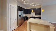 Located at 500 Blue Sky Dr in Concord, NC, this single-floor home offers a well-appointed layout designed for comfortable everyday living. The kitchen is a standout feature, showcasing rich dark cabinetry that extends to the ceiling, light granite countertops, stainless steel appliances including a gas range, built-in microwave, and refrigerator with ice maker, plus a central island with pendant lighting overhead. Hardwood flooring flows through the kitchen and living areas, lending warmth and continuity throughout the main living spaces. The living room is bright and inviting, highlighted by French doors with transom windows that open to an outdoor space, filling the room with natural light. A ceiling fan adds comfort to the space. The bedrooms feature plush carpeting and tray ceilings, with one bedroom offering a ceiling fan and a window with outdoor views, and another with direct access to a walk-in closet. The bathroom is finished with hardwood flooring, a dark vanity with a white countertop, a large mirror with bar lighting, and a tub-shower combination. A dedicated laundry room with a full-size side-by-side washer and dryer and overhead shelving adds everyday convenience to this thoughtfully designed home.
