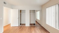 Located at 1699 E Washington St in Colton, California, this single-floor unit offers a well-organized layout designed for comfortable everyday living. Rich wood-style flooring runs throughout the space, providing a warm and cohesive aesthetic from room to room.

The open-concept living area is bright and generously proportioned, with neutral-toned walls and a pass-through window that connects seamlessly to the kitchen. This design detail enhances the sense of openness while maintaining a defined separation between living and cooking spaces.

The kitchen is efficiently laid out with warm wood cabinetry, light speckled countertops, and a full suite of black appliances including a refrigerator, electric range with microwave above, and a sink. A skylight overhead fills the kitchen with natural light, adding an airy quality to the space.

The bedroom is spacious and features dual sliding-door closets, offering ample storage. A window allows natural light in, and the room's neutral palette makes it easily adaptable.

The bathroom is clean and functional, featuring a wide vanity with speckled countertops and wood cabinetry, a large wall mirror, and a full tub-shower combination. Wood-style flooring continues here, maintaining design consistency throughout the unit.