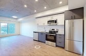 Located at 12322 102 Ave NW, this thoughtfully designed one-bedroom, one-bathroom unit offers a contemporary urban living experience within a compact, efficiently laid-out floor plan. The open-concept living and kitchen area is defined by a striking exposed concrete ceiling with recessed pot lighting, creating an industrial-modern aesthetic that is both bold and inviting. Light hardwood flooring runs throughout, lending warmth and continuity to every room.

The kitchen is well-appointed with a full suite of stainless steel appliances, including a French door refrigerator, electric range with over-the-range microwave, and dishwasher. Two-tone cabinetry pairs white upper cabinets with slate-grey lower cabinets, accented by a classic white subway tile backsplash and modern hardware. The open living area adjacent to the kitchen offers a versatile and airy space.

The bedroom is a quiet, functional retreat featuring a sliding-door closet with built-in shelving and a large window that frames views of the surrounding neighbourhood and city skyline, filling the room with natural light.

The bathroom is finished in a clean, modern style with grey cabinetry, a quartz-topped vanity, an undermount sink, black matte fixtures, and a round mirror. A connecting hallway provides practical separation between the living spaces and bedroom.