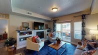 Located at 311 NW 96th St in Kansas City, MO, this single-floor residence offers a thoughtfully designed layout with a comfortable flow between living spaces. The living room serves as the heart of the home, anchored by a tiled fireplace with built-in shelving and a wall-mounted TV above. Sliding glass doors open to a private balcony, filling the room with natural light. Wood-style flooring runs throughout the main living areas, adding warmth and continuity. The dining area features an elegant chandelier overhead and ample space for a full dining set, positioned adjacent to the living room for easy entertaining. The kitchen is equipped with stainless steel appliances, including a range with over-the-range microwave, and is finished with white cabinetry and granite-style countertops. Two well-sized bedrooms each offer plush carpeting, ceiling fans, and windows that allow in natural light. Both bathrooms are finished with white vanity cabinetry, granite-style countertops, and wood-style flooring, each featuring a shower-tub combination. The overall design presents a neutral, warm palette with consistent finishes throughout, creating a cohesive and inviting living environment.
