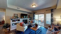 Located at 311 NW 96th St in Kansas City, MO, this single-floor residence offers a thoughtfully designed layout with a comfortable flow between living spaces. The living room serves as the heart of the home, anchored by a tiled fireplace with built-in shelving and a wall-mounted TV above. Sliding glass doors open to a private balcony, filling the room with natural light. Wood-style flooring runs throughout the main living areas, adding warmth and continuity. The dining area features an elegant chandelier overhead and ample space for a full dining set, positioned adjacent to the living room for easy entertaining. The kitchen is equipped with stainless steel appliances, including a range with over-the-range microwave, and is finished with white cabinetry and granite-style countertops. Two well-sized bedrooms each offer plush carpeting, ceiling fans, and windows that allow in natural light. Both bathrooms are finished with white vanity cabinetry, granite-style countertops, and wood-style flooring, each featuring a shower-tub combination. The overall design presents a neutral, warm palette with consistent finishes throughout, creating a cohesive and inviting living environment.
