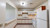 Located at 3350 Rue St Catherine St in Florissant, Missouri, this single-floor unit offers a straightforward and practical layout designed for comfortable everyday living. The kitchen is well-appointed with an abundance of white cabinetry trimmed in wood-tone accents, providing ample storage and counter space. A double-basin sink, electric range, and full-size refrigerator are included, and the room is finished with neutral tile flooring and ceiling lighting. A built-in pass-through shelf connects the kitchen to the adjacent living area, adding a functional architectural detail. The living and bedroom spaces feature wall-to-wall carpeting in a neutral tone, clean white walls, and wood baseboard trim throughout. Windows fitted with horizontal blinds allow natural light to filter into the rooms. The bathroom includes a full-size soaking tub and shower combination with a handheld showerhead, chrome grab bars, and clean white surround — practical and easy to maintain. The overall design of the unit is clean, neutral, and move-in ready, with consistent finishes throughout that create a cohesive and functional living environment.