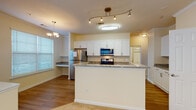 This single-floor residence is thoughtfully designed with a cohesive, neutral color palette and a mix of hard and soft flooring throughout. The kitchen serves as a central highlight, showcasing white shaker-style cabinetry, granite countertops, and a full suite of stainless steel appliances including a gas range, over-the-range microwave, and refrigerator. A peninsula with matching granite provides additional prep space and separates the kitchen from the living area, which features warm hardwood-style flooring and crown molding details. Track lighting and a flush-mount fixture illuminate the kitchen, while a chandelier adds a decorative touch nearby. A hallway leads to the carpeted living room, which benefits from natural light through sliding glass doors fitted with vertical blinds. The bedrooms are spacious and carpeted, each with windows that invite natural light, and one features a ceiling fan. The bathrooms are well-appointed with white tile tub-shower combinations accented by a decorative tile border, white cabinetry, granite vanity countertops, and wood-style flooring. The overall ambiance is clean, bright, and move-in ready.