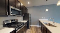 Located at 1000 Solomon Sq in Delaware, Ohio, this single-floor residence offers a well-designed layout with modern finishes throughout. The kitchen is a standout feature, equipped with rich dark cabinetry, stainless steel appliances including a gas range, built-in microwave, and refrigerator, complemented by light quartz countertops and a undermount sink with a sleek gooseneck faucet. Pendant lighting accents the kitchen peninsula, which opens to the main living area for a seamless, open-concept feel. The living area is generously proportioned, featuring wood-look luxury vinyl plank flooring and a set of French doors that invite natural light and provide views of the outdoors. The bedrooms are carpeted for comfort and feature neutral tones, large windows that bring in natural light, and access to well-appointed bathrooms. The bathrooms include dark vanity cabinetry with quartz countertops and a tub-shower combination. One bathroom connects directly to a bedroom and features a walk-through closet with built-in shelving. Throughout the residence, neutral gray walls, white trim, and consistent flooring selections create a cohesive, contemporary aesthetic that is both functional and inviting.
