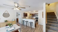 Located at University Suites in Greenville, NC, this 3-bedroom, 3-bathroom residence is spread across three floors, offering a well-organized and functional layout. The entry level features a combined dining and living area with wood-look flooring, ceiling fans, and large windows that invite natural light and views of the surrounding greenery. The adjacent kitchen is equipped with dark espresso cabinetry, granite-style countertops, stainless steel appliances including a refrigerator, range, and microwave, and a peninsula with bar seating — ideal for casual dining. A pantry provides additional storage convenience. The main living room is a standout space, boasting soaring vaulted ceilings, a ceiling fan, and a large picture window framing outdoor views, creating an open and airy atmosphere. Wood-look flooring flows consistently throughout the common areas. The three bedrooms each include dedicated closets and private bathrooms with tub-shower combinations and granite-style vanities. The upper floor features a bedroom with a charming angled ceiling, adding architectural character. Additional amenities include a laundry area, multiple staircases connecting each floor, and ample closet space throughout — delivering a comprehensive and comfortable living experience.