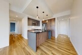 Located at 10620 99 Avenue NW in Edmonton's vibrant Oliver neighbourhood, this modern 3-bedroom, 2-bathroom unit offers a thoughtfully designed layout across a single floor. Light-toned hardwood flooring flows throughout the living spaces, complementing the clean, contemporary aesthetic found in every room.

The open-concept kitchen is a standout feature, showcasing warm walnut cabinetry paired with dark upper cabinets and a bold dark-topped island with an undermount sink and a sleek industrial-style faucet. Stainless steel appliances, a white tile backsplash, and elegant pendant lighting complete the polished look. The kitchen flows naturally toward the hallway and living areas, creating an efficient and connected layout.

Floor-to-ceiling windows in the living area and bedrooms flood the space with natural light and frame impressive panoramic views of Edmonton's downtown skyline. The bedrooms feature a neutral palette with grey accent walls and light hardwood floors, creating a calm and functional atmosphere. The primary bedroom benefits from a sliding door leading to a closet.

Both bathrooms are finished in tile, with one featuring a soaker tub and subway-tiled surround with a decorative mosaic accent stripe and a walnut vanity with a white countertop, providing a refined and functional finish throughout.