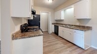 This single-floor residence at 415 W Northfield Blvd in Murfreesboro, Tennessee, offers a well-organized layout with a comfortable mix of wood-look vinyl and carpeted flooring throughout. The entry area features durable wood-look vinyl flooring and opens directly toward the kitchen, providing a seamless flow from the front door into the living spaces. The kitchen is fully equipped with white cabinetry, dark granite-style countertops, black appliances including an electric range, dishwasher, and refrigerator, all set atop matching wood-look vinyl flooring that adds continuity to the space. The living area is bathed in natural light through a large sliding glass door fitted with vertical blinds, offering views of the outdoors and providing direct exterior access. Carpeted bedrooms offer a cozy retreat, with one featuring a generously sized walk-in closet with built-in shelving for ample storage. A dedicated bedroom also includes a window allowing natural light to filter in. The bathroom is well-appointed with a dual-sink vanity topped with dark countertops, white cabinetry below, a large wall mirror, and a full shower-tub combination. Textured ceilings are consistent throughout, and neutral warm-beige walls create a cohesive, move-in-ready atmosphere across all areas of this single-level home.