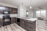 This single-floor unit offers a thoughtfully designed layout that balances functional living spaces with a clean, modern aesthetic. The kitchen serves as a central hub, showcasing rich dark-stained cabinetry paired with light stone-toned countertops and black appliances, including a range, microwave, dishwasher, and refrigerator. A peninsula with a double-basin sink and pendant lighting overhead connects the kitchen to the open living area, which features light wood-look flooring and a ceiling fan. Natural light filters in through windows offering elevated outdoor views of the surrounding area.

The bedrooms are carpeted and feature ceiling fans, baseboard heating, and windows that frame outdoor scenery. One bedroom includes a walk-in closet outfitted with wire shelving and hanging rods, providing generous storage capacity. Both bathrooms follow a consistent design language, each featuring dark wood vanities with light countertops, tile flooring, a tub-shower combination, and neutral wall tones. Panel-style white doors are used throughout, contributing to a cohesive and contemporary interior feel. The overall ambiance is clean, understated, and move-in ready.