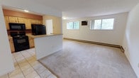 This single-floor, 1-bedroom, 1-bathroom unit is thoughtfully laid out to maximize functionality and comfort. The open-concept living area features neutral-toned carpet, a textured ceiling, and multiple windows that allow natural light to filter in while offering views of the surrounding greenery. A wall-mounted air conditioning unit and baseboard heating ensure year-round climate control throughout the space.

The kitchen is separated from the living area by a half-wall peninsula with a countertop overhang, providing a natural transition between spaces. It features light maple cabinetry with ample upper and lower storage, laminate countertops, a stainless steel sink, and a full suite of black appliances including an electric range, over-the-range microwave, dishwasher, and refrigerator. The kitchen is finished with easy-to-clean tile flooring.

The bedroom is a well-proportioned, carpeted room with a window that brings in natural light and is equipped with baseboard heating. The full bathroom includes a tub and shower combination with white tile surround, a toilet, and tile flooring, maintaining a clean and functional aesthetic throughout. The overall design of the unit is practical and move-in ready.