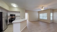 Located at 5600 22nd St N in Saint Petersburg, Florida, this single-story unit presents a clean, modern interior with a cohesive neutral color palette and light wood-look flooring extending throughout the space. The open-concept design connects the kitchen and living area seamlessly, creating a bright and functional floor plan.

The kitchen is well-appointed with white cabinetry, a subway tile backsplash, stainless steel appliances including a refrigerator, electric range, and microwave, and a peninsula featuring a white countertop that provides additional prep space and casual seating. A stainless steel sink with a modern faucet is integrated into the peninsula, and a ceiling-mounted light fixture illuminates the workspace.

The living area is generously sized and benefits from natural light through a window fitted with horizontal blinds. A ceiling fan with a light kit adds comfort and airflow. The layout also reveals entry doors, a closet, and hallway access leading to additional rooms.

The bedroom is a calm, well-proportioned room with a window overlooking greenery, providing natural light and a connection to the outdoors. The bathroom includes a full tub-shower combination with tile surround, a toilet, vanity, and wood-look flooring, finished with brushed nickel hardware and towel bars throughout.