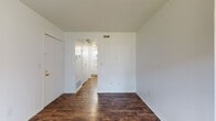 Located at 806 Grandview Pt in Dunbar, West Virginia, this single-floor residence offers a clean, straightforward layout finished with consistent dark hardwood-style flooring throughout. The crisp white walls and ceilings create a bright, neutral backdrop across all areas of the space.

The main living area is generously sized and benefits from a row of windows fitted with vertical blinds, allowing ample natural light to fill the room. A ceiling fan is centrally positioned overhead. An additional room features a sliding glass door that opens directly onto a private outdoor deck, providing views of surrounding mature trees and a seamless connection to the outdoors.

The layout, as seen in the overhead floor plan view, reveals a compact but functional arrangement of interconnected rooms, including a hallway corridor linking the living spaces to the private areas. The entry area includes closet access and connects efficiently to the rest of the unit.

The bathroom is equipped with a full-size soaking tub and shower combination, a white vanity with a yellow countertop and single-basin sink, a mirrored medicine cabinet, and a towel bar. The flooring continues the dark hardwood-style found throughout the rest of the space. Ventilation is provided via ceiling vents present in multiple rooms, and baseboard heating units are visible along the walls.