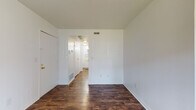 Located at 806 Grandview Pt in Dunbar, West Virginia, this single-floor residence offers a clean, straightforward layout finished with consistent dark hardwood-style flooring throughout. The crisp white walls and ceilings create a bright, neutral backdrop across all areas of the space.

The main living area is generously sized and benefits from a row of windows fitted with vertical blinds, allowing ample natural light to fill the room. A ceiling fan is centrally positioned overhead. An additional room features a sliding glass door that opens directly onto a private outdoor deck, providing views of surrounding mature trees and a seamless connection to the outdoors.

The layout, as seen in the overhead floor plan view, reveals a compact but functional arrangement of interconnected rooms, including a hallway corridor linking the living spaces to the private areas. The entry area includes closet access and connects efficiently to the rest of the unit.

The bathroom is equipped with a full-size soaking tub and shower combination, a white vanity with a yellow countertop and single-basin sink, a mirrored medicine cabinet, and a towel bar. The flooring continues the dark hardwood-style found throughout the rest of the space. Ventilation is provided via ceiling vents present in multiple rooms, and baseboard heating units are visible along the walls.