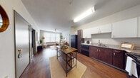 This single-floor residence offers a thoughtfully designed open-concept layout that seamlessly connects the kitchen and living areas. The kitchen is equipped with dark wood cabinetry, white upper cabinets, granite-style countertops, black appliances including a refrigerator, dishwasher, and range, and a double sink. A central island with bar seating adds both functionality and casual dining space. Rich hardwood-style flooring extends throughout the main living areas, lending warmth and continuity to the space.

The living room is bright and welcoming, featuring a large window that allows generous natural light to fill the room. The space comfortably accommodates a full seating arrangement and flows naturally from the kitchen.

The bedrooms are carpeted for comfort and each includes a window for natural light. One room is configured as a dedicated workspace, complete with a desk setup, carpeted flooring, and window with draping curtains.

Two full bathrooms serve the residence, each featuring a shower-tub combination with tiled surround, a dark wood vanity with a speckled countertop, and hardwood-style flooring. A textured ceiling is present throughout, and the neutral color palette creates a clean, cohesive aesthetic across all rooms.