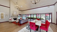 Located at 1600 Winters Creek Dr in Atlanta, GA, this single-floor clubhouse facility combines elegant design with practical amenities throughout its well-appointed spaces. The welcoming entrance foyer features warm hardwood-style flooring, recessed lighting, and glass sliding doors that flood the area with natural light and offer views of the surrounding landscaped grounds.

The centerpiece of the facility is a generously sized open-plan lounge and gathering area defined by soaring vaulted ceilings with rich burgundy crown molding accents. A dramatic floor-to-ceiling stacked stone fireplace anchors one wall, while an expansive wall of French doors along the opposite side frames sweeping views of the outdoor pool and patio area. Two statement chandelier fixtures provide warm overhead illumination. The space accommodates both a plush seating arrangement with a velvet sofa and armchairs set on a bold red patterned rug, and a separate dining area with a marble-top table and vivid red upholstered chairs.

The kitchen bar area is outfitted with a lengthy marble waterfall-edge island, cushioned bar seating with gold-accented bases, sage cabinetry with decorative tile backsplash, stainless steel appliances, and industrial pendant lighting. A dedicated private office nook features a patterned accent wall, a large desk, and red accent chairs, providing a professional and functional workspace. Throughout, the consistent use of burgundy trim, marble surfaces, and red accents creates a cohesive and sophisticated atmosphere.