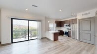 This well-appointed one-bedroom, one-bathroom residence offers a thoughtfully designed open-concept layout with modern finishes throughout. The combined living and kitchen area serves as the heart of the home, anchored by light-toned hardwood-style flooring that enhances the bright, airy ambiance. The kitchen is outfitted with rich dark-wood cabinetry, white quartz countertops, a subway tile backsplash, and a full suite of stainless steel appliances including a range, microwave, dishwasher, and refrigerator. A peninsula with an integrated sink provides additional prep space and casual seating. Pendant lighting accents the kitchen, while recessed lighting illuminates the living area. A large sliding glass door opens directly onto a private balcony, filling the space with natural light and offering open urban views. The bedroom features plush carpeting, a ceiling fan, and its own sliding glass door to the balcony, allowing for additional natural light and outdoor access. A dedicated closet provides convenient storage. The bathroom is finished with large-format tile flooring, a dark-wood vanity with a white countertop, and a glass-enclosed walk-in shower with subway tile surround and a rainfall showerhead, completing this refined and functional living space.