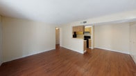 This single-floor residence offers a well-organized layout that balances comfort and functionality throughout its living spaces. The living area serves as the heart of the home, featuring warm hardwood-style flooring, neutral cream-toned walls, and a textured ceiling that carries through the entire space. A sliding glass door lined with vertical blinds fills the room with natural light while providing direct access to a private outdoor patio. The open sightlines connect the living area to a galley-style kitchen, which is equipped with warm oak cabinetry, a black electric range, a black refrigerator, and light-toned countertops. A pass-through counter opening creates a seamless connection between the kitchen and the main living space. The two bedrooms are carpeted in a neutral tan, offering a soft and quiet retreat. Each room features windows fitted with blinds that allow for natural light and privacy control. The textured ceilings are consistent throughout both rooms, lending a cohesive feel to the private quarters. Two full bathrooms serve the residence, each featuring a tiled tub-shower combination with chrome fixtures and clean white finishes. The overall aesthetic throughout the space is clean and neutral, providing a versatile canvas well-suited for a variety of décor styles.