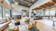 The Aventon Club House is a thoughtfully designed single-floor amenity space that seamlessly blends social, recreational, and professional functions. The main lounge serves as the centerpiece, featuring soaring ceilings with dramatic gold wire pendant chandeliers, exposed wood beam accents, and a soothing palette of soft blues, warm neutrals, and bold yellow accents. Light hardwood flooring and abstract patterned area rugs run throughout, tying the open-plan layout together cohesively. A comfortable seating area with plush sofas and mid-century modern chairs invites relaxed gatherings, while decorative wall art and sculptural floral wall pieces add artistic character. Adjacent to the lounge is a café-style bar area equipped with a coffee station, counter seating, and pendant lighting — ideal for casual meetups. The game room impresses with a full-size billiards table and shuffleboard, bathed in natural light from floor-to-ceiling windows overlooking the surrounding community. A private work suite offers a quiet retreat with a dedicated desk, task lighting, and a large window framing outdoor views. A windowed dining nook with pendant lighting provides an intimate setting. Throughout, large windows ensure the space is filled with natural light, creating a bright and welcoming atmosphere.