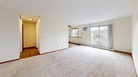 Located at 7635 Greenfield Ave in Mounds View, MN, this two-bedroom, one-bathroom unit offers a functional and comfortable single-floor layout. The open living room is a standout space, featuring large sliding glass doors that lead to a private balcony, filling the room with natural light. Neutral-toned carpet, a ceiling fan, and a wall-mounted AC unit complete the living area, which flows naturally into the rest of the unit. The kitchen and dining area are combined into one efficient space, showcasing dark cabinetry that contrasts cleanly against light countertops, a double sink, and a white appliance suite including a refrigerator and electric range. A ceiling fan overhead adds comfort to the dining end of the room, which benefits from an exterior-facing window. Both bedrooms are carpeted and bright, with warm wood-trimmed windows that let in generous natural light. The primary bedroom is notably spacious and features multiple windows with outdoor views. The full bathroom includes a tub-shower combination with built-in shelving and mosaic tile flooring. Throughout the unit, multiple closets and two hallways provide excellent storage. Baseboard heating is present throughout, ensuring year-round comfort.