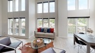 Located at 8500 Lake City Way NE in Seattle, WA, this architecturally distinctive loft-style unit offers an impressive sense of volume and openness. The living area commands immediate attention with its soaring double-height ceilings and a dramatic wall of oversized windows that flood the space with natural light and frame panoramic views of the surrounding neighborhood and greenery. Light hardwood flooring runs throughout, complementing the clean, neutral palette of the walls. A loft mezzanine level, accessible via a sleek ladder, adds a functional upper tier and enhances the vertical drama of the main living space. The kitchen features floor-to-ceiling dark cabinetry, black appliances, a full suite of modern fixtures, and a warm wood-paneled ceiling that adds a contrasting texture and coziness to the space. The dining area benefits from its own generous window arrangement with direct access to a private balcony, offering treetop and city views. The bedroom is a well-proportioned retreat with large windows, plush carpeting, and ample storage. Throughout the unit, the interplay of soaring ceilings, abundant natural light, modern finishes, and thoughtful design details creates a refined yet comfortable urban living environment.