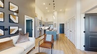 This single-story residence is defined by its dramatic, soaring ceilings that lend an expansive, airy quality throughout the open-concept living spaces. Light-toned hardwood flooring runs continuously through the main areas, connecting the living room, kitchen, and dining space in a seamless flow.

The kitchen is a standout feature, appointed with gray shaker-style cabinetry, white subway tile backsplash, granite countertops, and a full suite of stainless steel appliances including a side-by-side refrigerator, range, and built-in microwave. A large granite-topped island with a dark base provides seating for multiple guests and serves as a natural gathering point.

The living room benefits from tall double doors with a transom window above, allowing generous natural light to filter in. A bold navy accent wall adds visual depth near the kitchen-living transition.

The primary bedroom features plush carpeting, a bright window with outdoor views, and direct access to a spacious walk-in closet that connects to a well-appointed en suite bathroom with a glass-enclosed shower, granite vanity, and gray cabinetry. A second full bathroom mirrors the same cohesive design aesthetic with a tub-shower combination and matching finishes throughout.