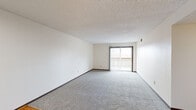 This single-floor, 2-bedroom, 2-bathroom unit is thoughtfully laid out to maximize its comfortable footprint. The living room serves as the heart of the space, featuring plush gray carpeting, neutral white walls, and a textured ceiling. A sliding glass door opens to a private balcony, filling the room with natural light and providing outdoor access. The transition from carpet to hardwood-style flooring marks the entry area near the front door, adding visual contrast and practicality.

The kitchen is compact yet efficient, featuring warm oak cabinetry, white countertops, a stainless steel sink, and wood-look flooring. It is equipped with a full-size refrigerator and dishwasher, offering all essential appliances within a well-organized space.

The primary bedroom is generously sized, with large windows that bring in natural light and views of the surrounding area. It includes a built-in closet with bifold doors, providing ample storage. The second bedroom is equally comfortable, with soft carpeting and bright, neutral walls.

The two bathrooms offer functional designs — one features a wall-mounted sink with a medicine cabinet mirror and tile flooring, while the other includes a full tub-shower combination. Two hallways connect the rooms seamlessly, rounding out this well-structured and practical living space.