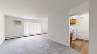 Located at 36250 Lakeshore Boulevard in Eastlake, Ohio, this single-floor, 3-bedroom unit offers a practical and straightforward layout with a connecting hallway. The living area is generously proportioned, featuring neutral gray carpeting, white walls, and a large sliding glass door fitted with vertical blinds that allows ample natural light to fill the room. A ceiling fan with a light fixture and a wall-mounted air conditioning unit provide year-round comfort, while baseboard heating runs along the exterior walls throughout the unit. The kitchen features warm wood cabinetry, a white range, and tile flooring, providing a functional workspace separate from the main living area. The expansive primary bedroom occupies a significant portion of the floor plan, offering substantial space for furnishings. Each bedroom is finished with the same gray carpet and white walls, and features a full-width bi-fold closet with dark wood panels and brass hardware. Individual windows with vertical blinds provide natural light and ventilation to the bedrooms, with wall-mounted AC units present in select rooms. The hallway connects the bedrooms efficiently, completing this well-organized single-level layout.
