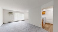 Located at 36250 Lakeshore Boulevard in Eastlake, Ohio, this single-floor, 3-bedroom unit offers a practical and straightforward layout with a connecting hallway. The living area is generously proportioned, featuring neutral gray carpeting, white walls, and a large sliding glass door fitted with vertical blinds that allows ample natural light to fill the room. A ceiling fan with a light fixture and a wall-mounted air conditioning unit provide year-round comfort, while baseboard heating runs along the exterior walls throughout the unit. The kitchen features warm wood cabinetry, a white range, and tile flooring, providing a functional workspace separate from the main living area. The expansive primary bedroom occupies a significant portion of the floor plan, offering substantial space for furnishings. Each bedroom is finished with the same gray carpet and white walls, and features a full-width bi-fold closet with dark wood panels and brass hardware. Individual windows with vertical blinds provide natural light and ventilation to the bedrooms, with wall-mounted AC units present in select rooms. The hallway connects the bedrooms efficiently, completing this well-organized single-level layout.