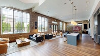 Located at 200 Resource Pkwy in Franklin, Tennessee, this single-floor communal living space offers a well-appointed and generously sized interior that blends industrial charm with modern comfort. The space is defined by striking exposed brick walls that stretch toward soaring vaulted ceilings, creating an open, airy atmosphere throughout.

Abundant natural light pours in through oversized floor-to-ceiling steel-framed windows, offering views of an outdoor pool area and lush landscaping. Rich hardwood-style flooring runs throughout, anchoring the warm, inviting aesthetic.

The living area is thoughtfully arranged with multiple seating vignettes, including leather sofas, upholstered accent chairs, and natural wood coffee tables, providing flexible spaces for both relaxation and socializing. A bold, vintage Purity Dairy mural serves as a compelling focal point on one of the brick accent walls, adding local Nashville-area character to the space.

A dedicated game area features a full-size billiards table beneath a modern pendant light, complemented by a wall-mounted flat-screen television. A staircase with a clean white surround adds architectural interest along the rear brick wall, while curated artwork and decorative objects throughout reflect a refined, creative sensibility. The overall ambiance is sophisticated yet welcoming, ideal for gathering and community engagement.
