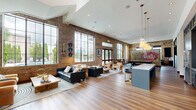 Located at 200 Resource Pkwy in Franklin, Tennessee, this single-floor communal living space offers a well-appointed and generously sized interior that blends industrial charm with modern comfort. The space is defined by striking exposed brick walls that stretch toward soaring vaulted ceilings, creating an open, airy atmosphere throughout.

Abundant natural light pours in through oversized floor-to-ceiling steel-framed windows, offering views of an outdoor pool area and lush landscaping. Rich hardwood-style flooring runs throughout, anchoring the warm, inviting aesthetic.

The living area is thoughtfully arranged with multiple seating vignettes, including leather sofas, upholstered accent chairs, and natural wood coffee tables, providing flexible spaces for both relaxation and socializing. A bold, vintage Purity Dairy mural serves as a compelling focal point on one of the brick accent walls, adding local Nashville-area character to the space.

A dedicated game area features a full-size billiards table beneath a modern pendant light, complemented by a wall-mounted flat-screen television. A staircase with a clean white surround adds architectural interest along the rear brick wall, while curated artwork and decorative objects throughout reflect a refined, creative sensibility. The overall ambiance is sophisticated yet welcoming, ideal for gathering and community engagement.