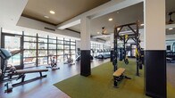 Located at 1625 Santa Venetia St in Chula Vista, CA, this single-floor fitness center is a comprehensive and thoughtfully designed wellness facility. The space is organized into distinct training zones, each tailored to a specific type of workout.

The cardio area is lined with floor-to-ceiling, industrial-style glass windows that flood the room with natural light while offering views of the surrounding outdoor environment. It is equipped with a full row of treadmills, ellipticals, and upright and recumbent stationary bikes, including Life Fitness branded machines.

The functional training zone features a large multi-station rig with TRX suspension trainers, a punching bag, barbell storage with weight plates, and a Hammer Strength functional trainer — all set atop green turf flooring. Ceiling fans overhead keep the space comfortable during high-intensity sessions.

A dedicated strength area houses a cable machine and a rack of dumbbells against a deep teal accent wall, providing a focused environment for resistance training.

The studio space features rich hardwood-style flooring, a tray ceiling with recessed lighting, full-length mirrors, stability balls, TRX accessories, and kettlebells — ideal for group classes or individual training. A dramatic arched window in the strength room adds an architectural flourish, complementing the modern, upscale aesthetic throughout.