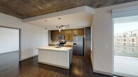 This contemporary single-floor residence showcases an industrial-modern aesthetic defined by striking exposed concrete ceilings, rich dark hardwood flooring, and clean white walls throughout. The open-concept living and dining area is spacious and airy, filled with natural light from large sliding glass doors that lead to a private balcony overlooking the surrounding cityscape.

The kitchen is a standout feature, outfitted with rich dark-stained cabinetry, a light quartz countertop island with an undermount sink, stainless steel appliances including a French door refrigerator and electric range, a subway tile backsplash, and pendant lighting paired with adjustable track lighting overhead.

The bedrooms continue the exposed concrete ceiling detail, each equipped with a ceiling fan and large windows that invite natural light and offer views of the city and surrounding greenery. Structural concrete columns add an architectural character to the rooms.

Two bathrooms feature light tile flooring, wood-toned vanities with quartz countertops, and framed mirrors. The primary bathroom includes a soaking tub with large-format tile surround and a double-sink vanity. A dedicated laundry closet with a stacked washer and dryer provides added convenience. Together, these elements create a cohesive urban living experience with refined, functional design.
