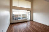 This two-story residence offers a well-designed layout that efficiently combines function and modern style across two distinct levels. The main floor centers around an open-plan living and kitchen area, where warm hardwood flooring flows throughout. The kitchen is equipped with stainless steel appliances, including a gas range, over-the-range microwave, refrigerator, and dishwasher. A marble-style granite countertop island serves as both a workspace and casual dining surface, accented by a pendant light overhead. A sleek tile backsplash in a linear mosaic pattern adds a refined touch behind the range. Dark wood cabinetry provides ample storage and contributes to the kitchen's contemporary aesthetic. Natural light filters in through a window at the end of the living area, brightening the open space. A powder room on the main floor features a wall-mounted sink, toilet, and wood-look flooring. The open-tread staircase, framed with a steel railing and warm wood handrail, leads to the upper level, where carpeted flooring and a half-wall overlook create a flexible loft-style space suitable for use as a sleeping area or home office. A full bathroom with a soaking tub and shower completes the upper floor, maintaining the clean, neutral palette found throughout the residence.