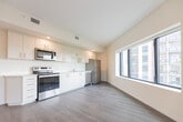 Located at 387 King St E in Kitchener, Ontario, this thoughtfully designed 2-bedroom, 1-bathroom unit offers a clean, contemporary aesthetic across a single floor. The layout flows efficiently from a welcoming hallway into the main living areas, all finished with light-toned laminate hardwood flooring and crisp white walls that create a bright, cohesive feel throughout.

The open-concept living and kitchen area is a standout feature, anchored by a large multi-pane window that invites abundant natural light and frames views of the surrounding urban neighbourhood. The kitchen is equipped with stainless steel appliances, white cabinetry, and ample counter space, making it both functional and visually appealing.

Both bedrooms are well-proportioned and finished with the same hardwood-style flooring. Each room benefits from large black-framed windows that offer treetop and neighbourhood views, filling the spaces with natural light. The primary bedroom provides a comfortable footprint ideal for a full furniture arrangement.

The bathroom is finished with large-format grey floor tiles, a white vanity with under-cabinet storage, a backlit mirror, and a separate shower and toilet area, delivering a clean and practical design.

Overall, the unit presents a modern, move-in-ready space with consistent finishes, efficient use of space, and a bright, airy ambiance suited to urban living in the heart of Kitchener.
