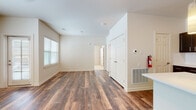 This single-story unit is designed with a clean, contemporary aesthetic, featuring warm wood-style luxury vinyl flooring that flows consistently throughout the main living areas. The open-concept living and dining space is bright and welcoming, with multiple windows fitted with horizontal blinds that allow natural light to fill the room. A ceiling fan adds both function and comfort to the space.

The kitchen is a standout feature, equipped with dark espresso cabinetry, white quartz countertops, a white subway tile backsplash, and a full suite of stainless steel appliances including a refrigerator, electric range, microwave, and dishwasher. A peninsula island with an integrated sink and pendant lighting above provides additional prep space and casual seating potential.

The bedroom is finished with soft, neutral carpeting, offering a comfortable contrast to the hard flooring in the main areas. The bathroom features a dark vanity with white countertop, wood-style flooring, a soaking tub, and clean white walls. Additional practical details throughout include a wall-mounted thermostat, floor vents, and a double-door closet.