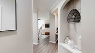 This single-story residence offers a thoughtfully designed layout with a cohesive neutral palette and wood-look flooring carried throughout. The entryway corridor makes a strong first impression, featuring an elegant arched built-in display niche and structural columns that frame the transition into the main living areas. A decorative woven pendant light adds a stylish touch at the entry.

The living room is well-proportioned, featuring crown molding, a ceiling fan, and a window that brings in natural light. Built-in shelving with an arched surround adds functional character to the space. Adjacent to the living area, the dining space accommodates a table beneath a large window dressed with curtains.

The kitchen is outfitted with white shaker-style cabinetry, white quartz-style countertops, a subway tile backsplash, and a full suite of stainless steel appliances, including a refrigerator, range, microwave, and dishwasher.

The bedrooms offer comfortable proportions, natural light from windows with blinds, and ceiling fans in select rooms. The bathroom features a tub-shower combination, white vanity cabinetry, and a large mirror. A dedicated laundry room with side-by-side washer and dryer connections adds everyday convenience.