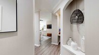 This single-story residence offers a thoughtfully designed layout with a cohesive neutral palette and wood-look flooring carried throughout. The entryway corridor makes a strong first impression, featuring an elegant arched built-in display niche and structural columns that frame the transition into the main living areas. A decorative woven pendant light adds a stylish touch at the entry.

The living room is well-proportioned, featuring crown molding, a ceiling fan, and a window that brings in natural light. Built-in shelving with an arched surround adds functional character to the space. Adjacent to the living area, the dining space accommodates a table beneath a large window dressed with curtains.

The kitchen is outfitted with white shaker-style cabinetry, white quartz-style countertops, a subway tile backsplash, and a full suite of stainless steel appliances, including a refrigerator, range, microwave, and dishwasher.

The bedrooms offer comfortable proportions, natural light from windows with blinds, and ceiling fans in select rooms. The bathroom features a tub-shower combination, white vanity cabinetry, and a large mirror. A dedicated laundry room with side-by-side washer and dryer connections adds everyday convenience.