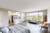 Located at 120 W Third Ave in San Mateo, CA, this efficiently designed studio offers a thoughtfully organized single-floor layout comprising a living area, kitchen, and bathroom. The open-concept living space is anchored by expansive floor-to-ceiling picture windows that flood the interior with natural light and frame sweeping treetop and hillside views — a standout feature of the unit. Light hardwood-style flooring runs throughout, contributing to a clean, cohesive aesthetic.

The kitchen is well-appointed with white shaker cabinetry, dark countertops, subway tile backsplash, and a full suite of stainless steel appliances including a refrigerator, microwave, range, and dishwasher. A breakfast bar with seating connects the kitchen to the main living area, making the space feel open yet functionally defined.

The living area is versatile, accommodating both sleeping and lounge zones with ease. Neutral warm-gray walls and airy white ceilings enhance the sense of openness. The bathroom features a clean, minimal design with dark wood cabinetry, a mirrored medicine cabinet, white tile, and brushed nickel fixtures. Overall, the space offers a modern, light-filled environment well-suited for comfortable urban living in the heart of San Mateo.
