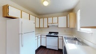 Located at 2800 Booty Dr in Columbus, Ohio, this two-story residence offers a straightforward and functional layout across two levels. The kitchen is a standout feature, showcasing an L-shaped design with abundant white cabinetry trimmed in warm wood accents, providing generous storage throughout. White appliances — including a gas range and a full-size refrigerator — complement the light countertops, while a stainless steel sink adds a practical touch. Dark hardwood-style flooring grounds the kitchen and creates a pleasant contrast with the lighter cabinetry and walls. An overhead range hood is centrally positioned for ventilation, and a ceiling-mounted light fixture provides ample illumination. The textured ceiling adds a classic residential character to the space. Overall, the kitchen is designed with efficiency in mind, making excellent use of its footprint. The two-floor layout suggests additional living, dining, and sleeping spaces that carry through the same practical and welcoming aesthetic, making this Columbus property a solid and functional place to call home.