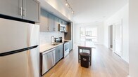 Located at 916 West St in Charlottesville, Virginia, this single-floor unit offers a thoughtfully designed open layout that seamlessly connects the kitchen and living areas. The kitchen is a standout feature, showcasing slate-gray shaker-style cabinetry paired with a white subway tile backsplash and light granite countertops. A full suite of stainless steel appliances — including a refrigerator, electric range, built-in microwave, and dishwasher — provides modern functionality, while track lighting overhead ensures excellent illumination. Light-toned hardwood-style flooring runs throughout the main living areas, enhancing the sense of openness and warmth.

The living area is bright and airy, benefiting from a large window that invites natural light and offers views of the surrounding neighborhood. The space flows naturally toward the bedroom area, which includes a walk-in closet and additional storage behind louvered doors. The bathroom is clean and modern, featuring a soaking tub with shower combination, brushed gold fixtures, tile flooring, and a granite-topped vanity. The overall aesthetic is contemporary and cohesive, with crisp white walls and carefully selected finishes throughout.